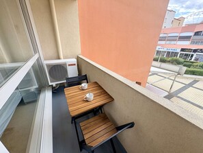 A balcony with a table and chairs, an air conditioning unit, and a view of buildings. - Studio in Cap d'Agde center - 2 guests (Cap d'Agde)