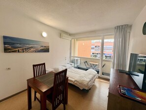 Ein Hotelzimmer mit Bett, Schreibtisch, Sessel, Fernseher und Fenster mit Blick auf Gebäude.