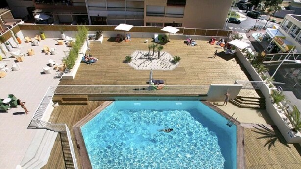 A rooftop pool with a wooden deck, lounge chairs, and umbrellas. - Studio in Cap d'Agde center - 2 guests (Cap d'Agde)