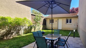 An outdoor patio with a glass table and chairs, a large umbrella, and a tiled floor. - Unique house for car enthusiasts (Chenicourt)