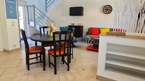 A dining area with a table and chairs, a staircase, a sofa, and a wall-mounted TV. - Unique house for car enthusiasts (Chenicourt)