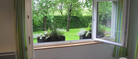 A dining area with a table set for two, a window with a view of a garden, and a chair.