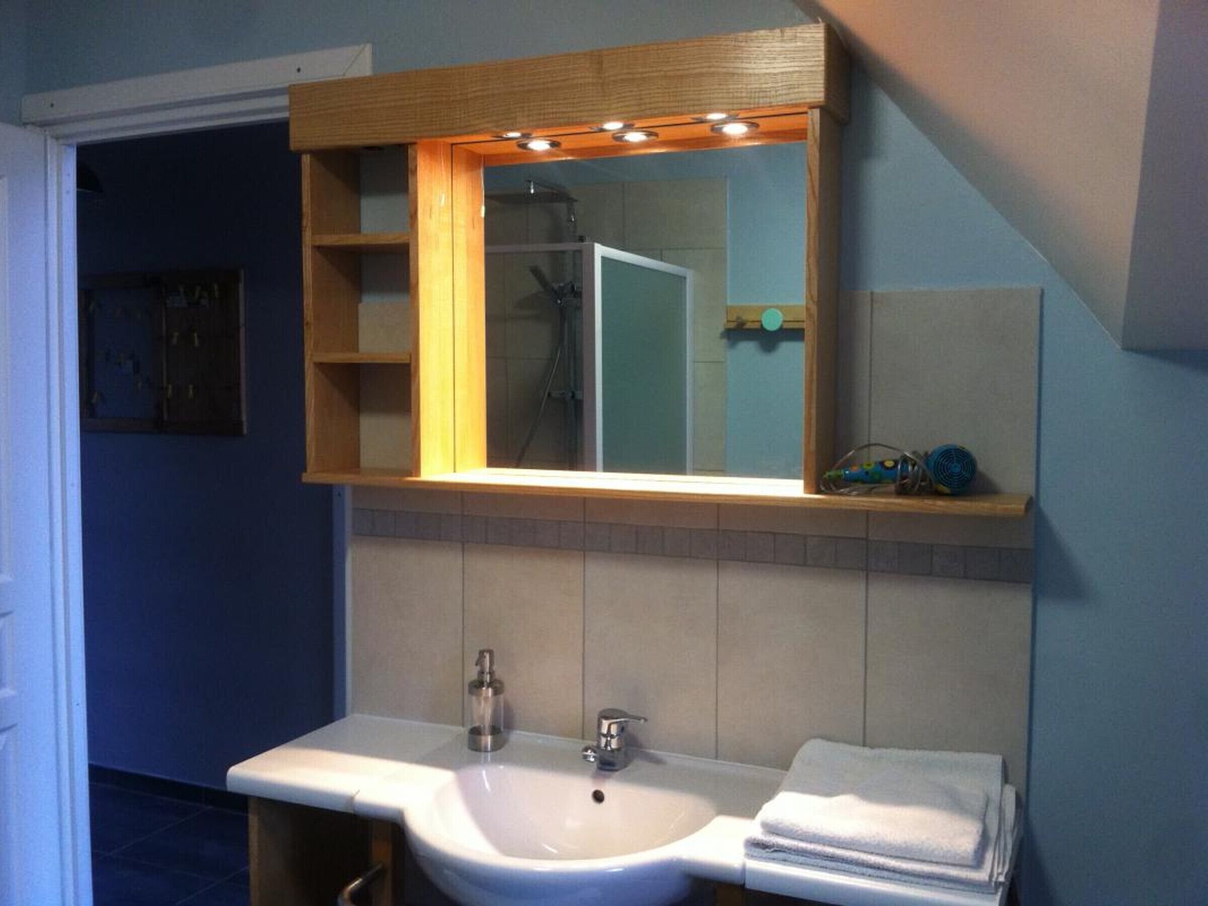 A bathroom with a white sink, a mirror, and a shower visible in the reflection.