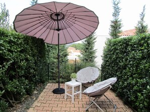 Eine Terrasse mit großem Sonnenschirm, einem weißen Tisch und einem Klappstuhl.