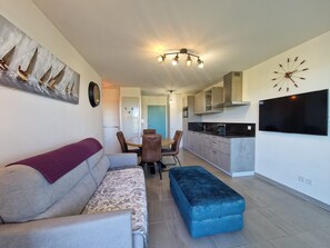 Ein modernes Wohnzimmer mit einer Couch, einem Hocker und einem Esstisch mit Stühlen.