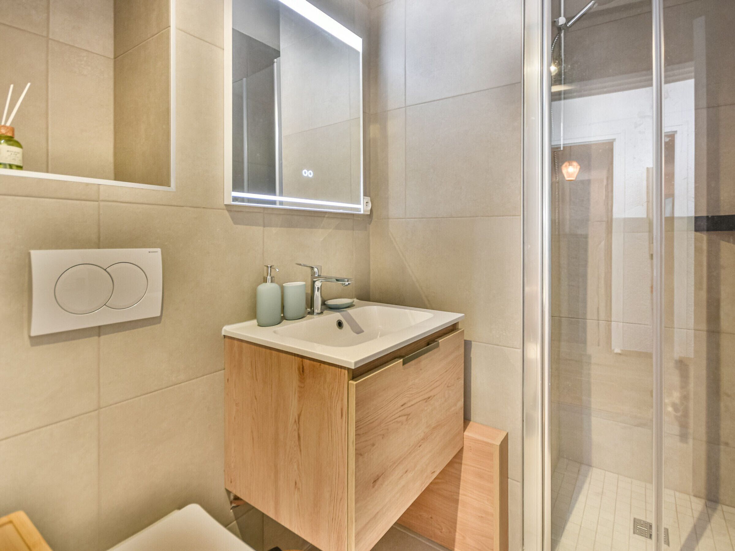 A modern bathroom with a wooden vanity, a glass shower enclosure, and a wall-mounted mirror.