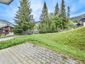 A paved pathway leading to a building with a balcony, surrounded by trees and a small bridge. - Charming apartment near slopes - 7 guests (Les Gets)