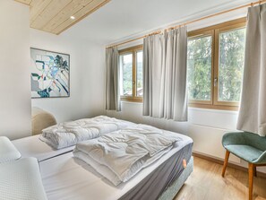 A bedroom with a bed, a chair, a window with curtains, and a painting on the wall. - Charming apartment near slopes - 7 guests (Les Gets)