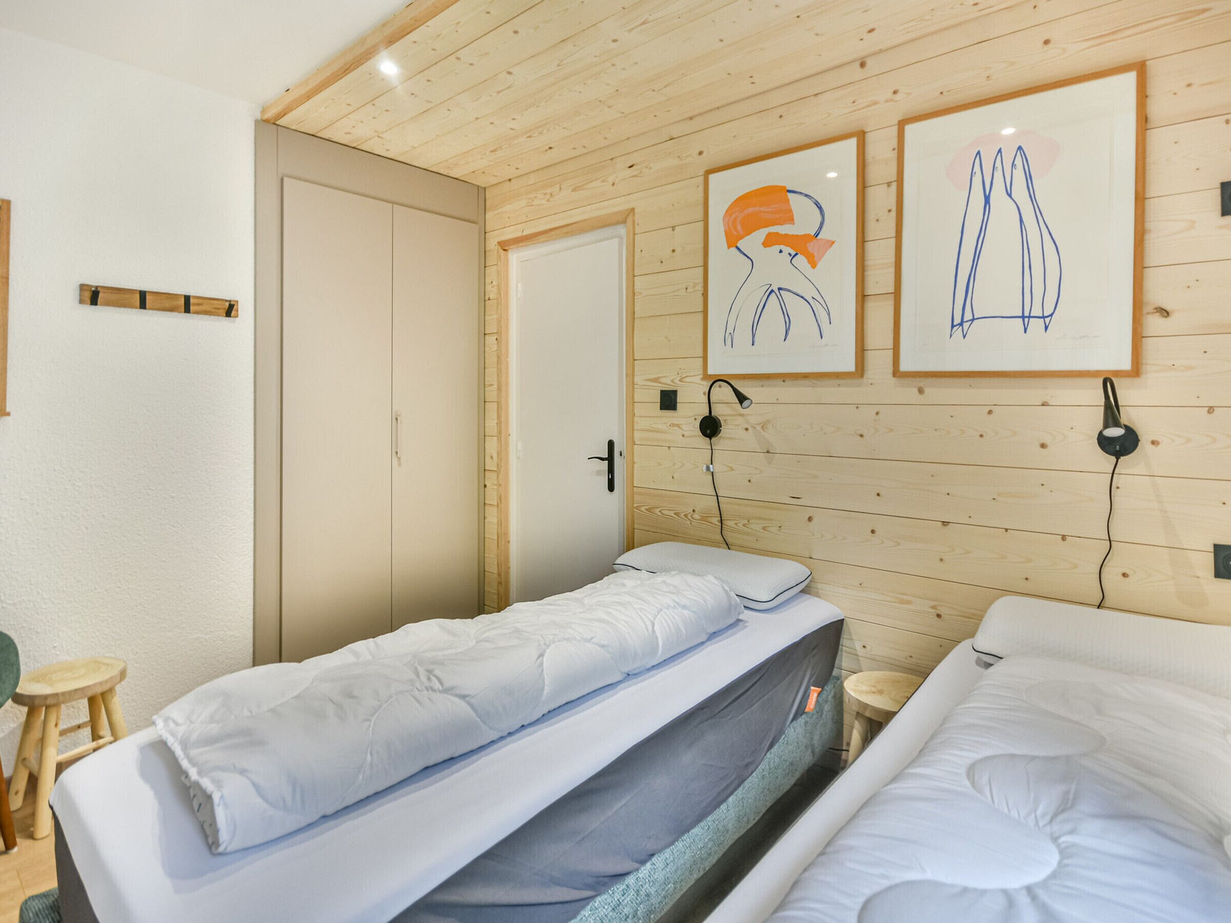 A room with two beds, wooden walls, a door, and two framed artworks.