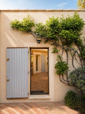 Ein Gebäudeeingang mit Holztür, einer gefliesten Terrasse und einer Wand mit Kletterpflanzen.
