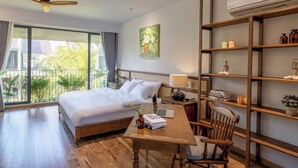 Ein Hotelzimmer mit Bett, Schreibtisch mit Stuhl, Bücherregal und einem großen Fenster mit Blick ins Grüne.
