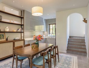 A modern kitchen with a dining table, chairs, and a hanging light fixture. - Hometown Pinky 3 BRS Pool Villa Hoi An (Hoi An Tay)