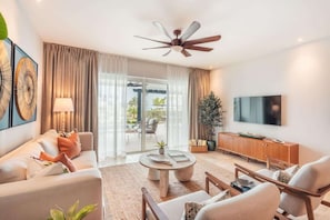 A modern living room with a ceiling fan, a television, and a sliding glass door leading to an outdoor area. - Apex Executive Apartments - Monterrico (Monterrico)