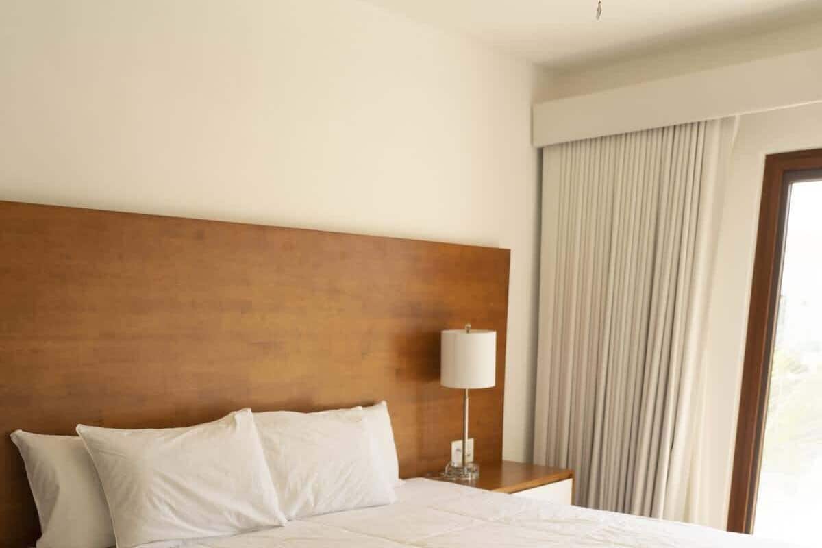 Una cama grande con cabecera de madera, ropa de cama blanca y una mesita de noche con lámpara.