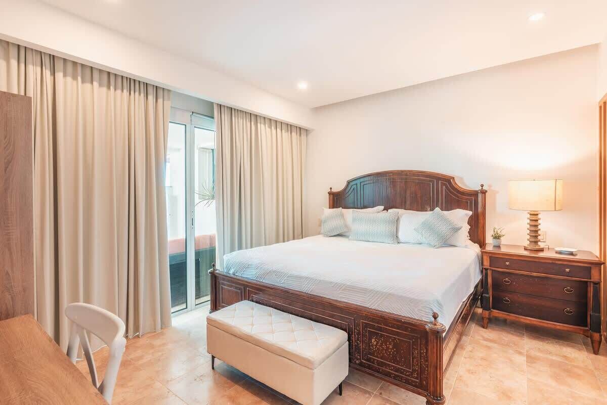 A bedroom with a wooden bed, a bedside table, a chair, and a window with curtains.