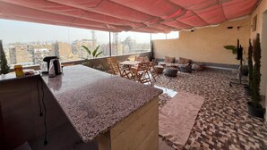 A rooftop terrace with a kitchen area, seating, and a view of the cityscape. - Green Hostel (Cairo)