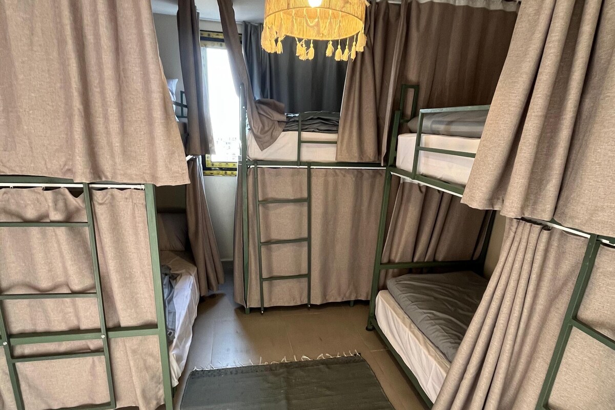 Een slaapkamer met stapelbedden, gordijnen, een ladder en een hanglamp.