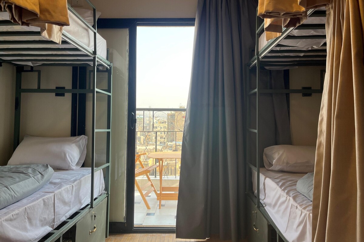 Een slaapzaal met stapelbedden, een schuifdeur naar een balkon en uitzicht op de omgeving.