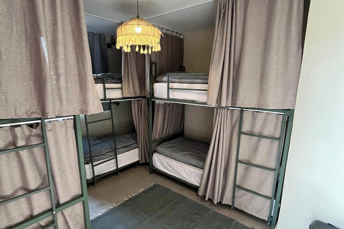 Een slaapzaal met stapelbedden, een hanglamp en een klein vloerkleed.