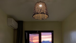 A hotel room with a bed, a window with a cityscape view, a hanging light fixture, and an air conditioning unit. - Green Hostel (Cairo)