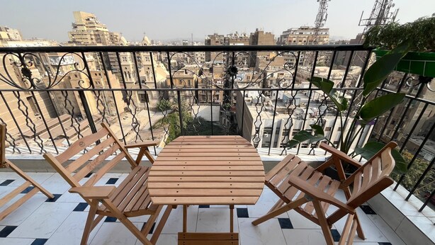 A balcony with a wooden table and chairs, a tiled floor, and a view of the cityscape. - Green Hostel (Cairo)