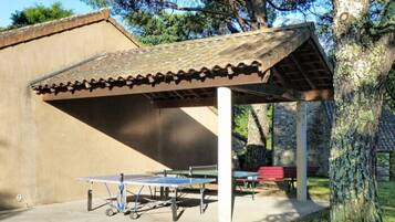 An outdoor pavilion with a roof, a table tennis table, and benches.