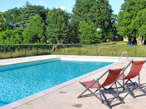A swimming pool with a clear blue water surface, surrounded by a concrete deck. There are two lounge chairs with red cushions. - Mezzanine Cottage Stay in Ardeche for 4 (Chambonas)
