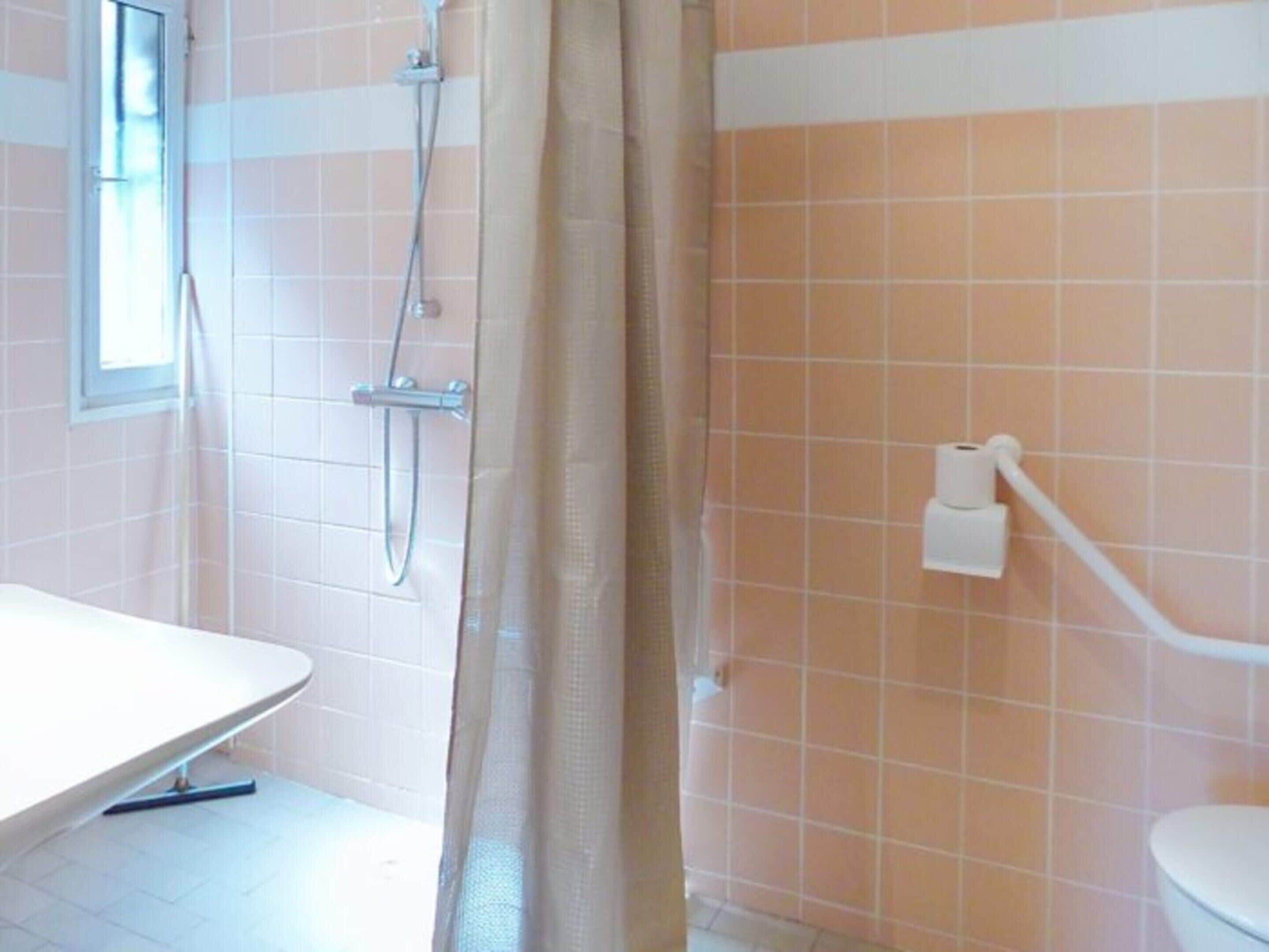 Een badkamer met douche, toilet en een raam.