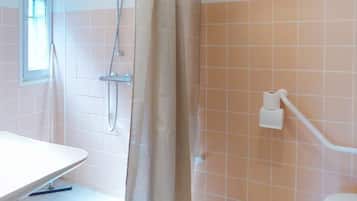 Een badkamer met douche, toilet en een raam.