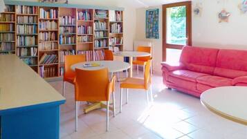Una habitación con una estantería, un sofá rosa y una zona de comedor con sillas naranjas.
