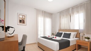 A hotel room with a bed, a desk with a telephone, a chair, and a bedside table with a lamp and a plant. - Villa Amarilia - 100m from Pernera Beach (Pernera)