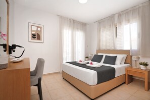 Une chambre d’hôtel comprenant un lit, un bureau avec un téléphone, une chaise et une table de chevet avec une lampe et une plante.