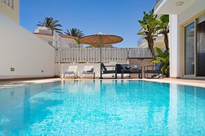 A swimming pool with lounge chairs and an umbrella, surrounded by a white fence and palm trees. - Villa Amarilia - 100m from Pernera Beach (Pernera)