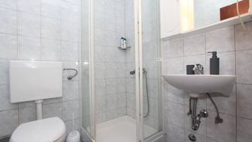 Une salle de bain comprenant des toilettes, une douche fermée par une paroi de verre et un lavabo avec un robinet.