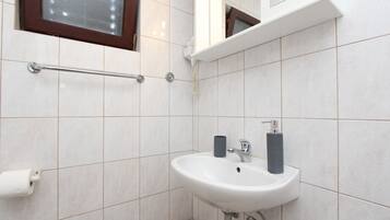 A bathroom with white tiles, a white sink with two soap dispensers, a handrail, and a toilet paper holder.