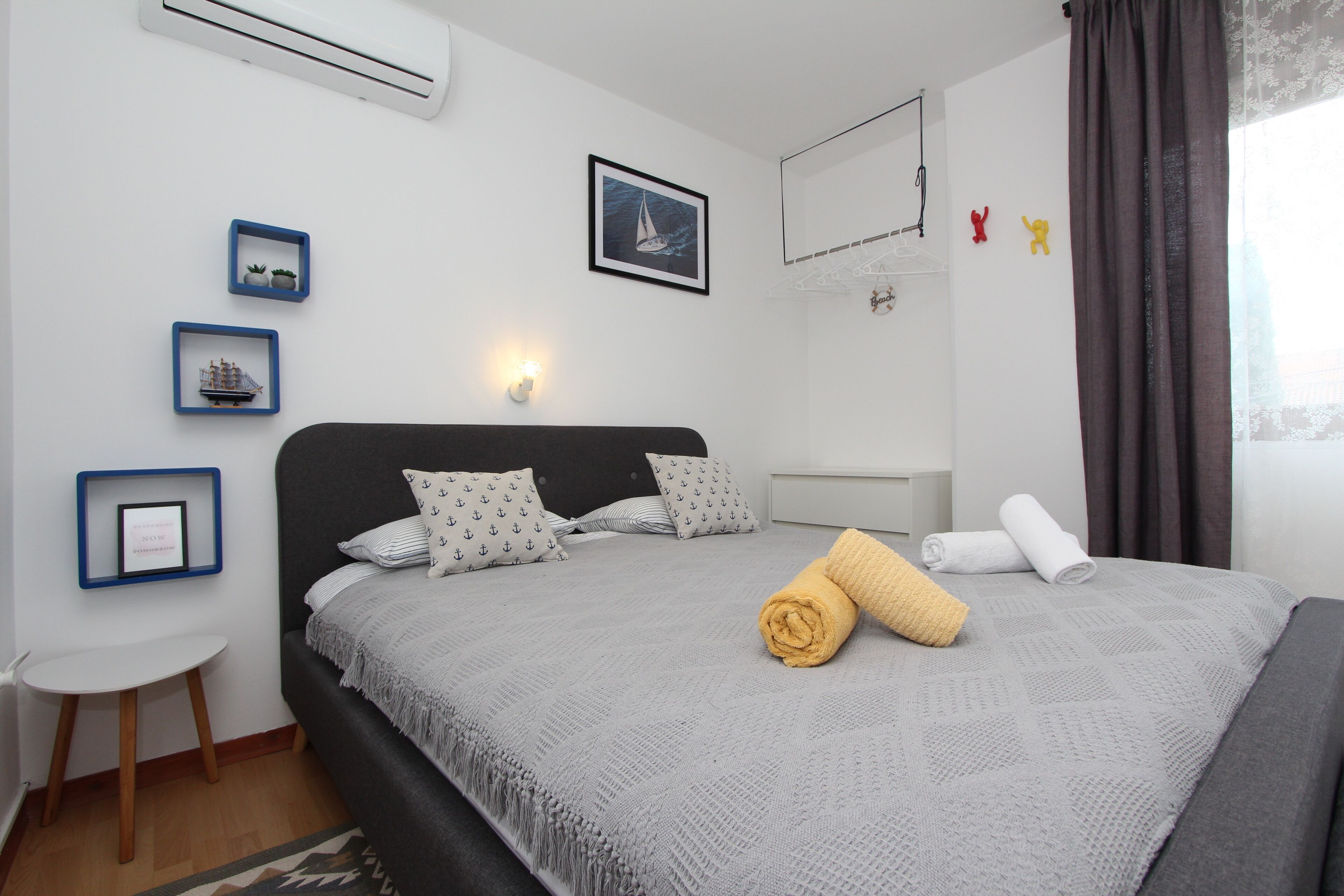 Une chambre à coucher bien rangée, avec un lit, une petite table et des éléments de décoration murale, notamment des tableaux encadrés et une étagère fixée au mur.