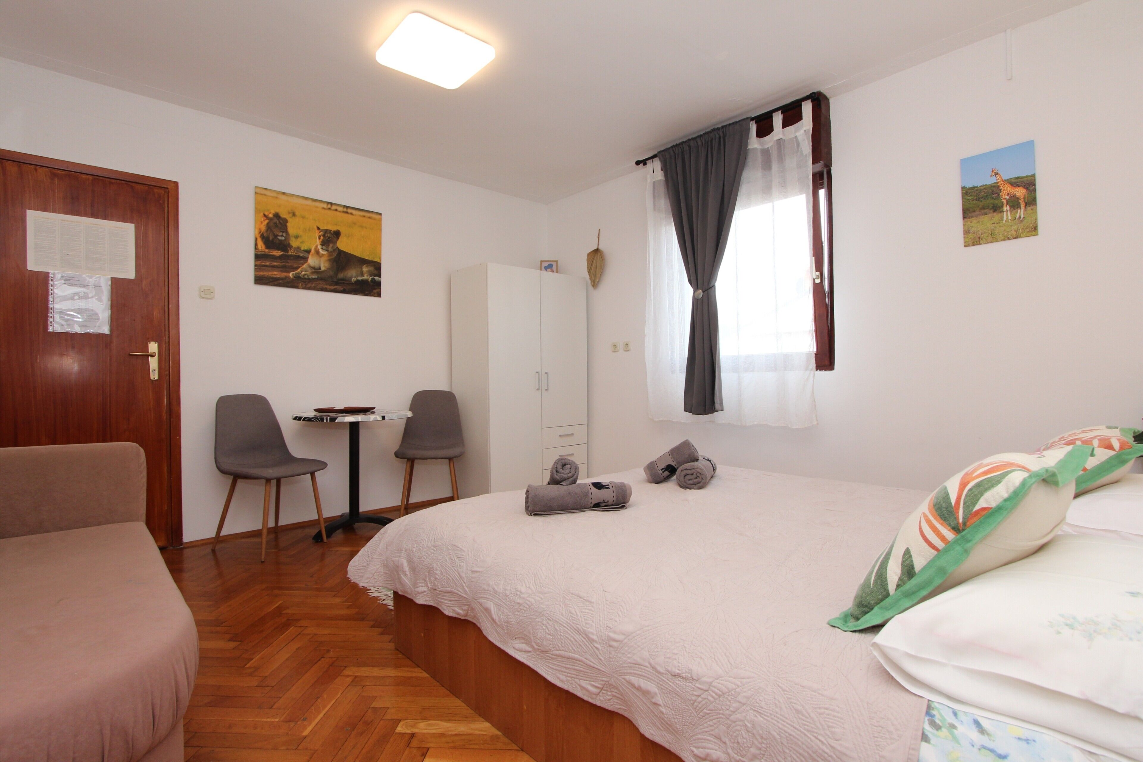A bedroom with a bed, a desk, two chairs, a wardrobe, and a door with a notice.