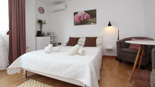 A neatly made bed with rolled towels, a grey armchair, a small round table, and a wall-mounted air conditioner. - Rooms and Studio Salvi (Rovinj)