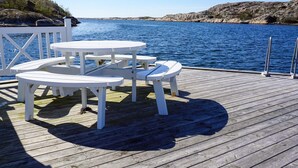 A wooden deck with white picnic tables overlooking a body of water. - 4 Star Holiday Home in Kungshamn (Kungshamn)