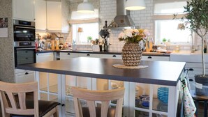A kitchen with white cabinets, a central island with chairs, pendant lights, and a decorative pineapple vase. - 4 Star Holiday Home in Kungshamn (Kungshamn)