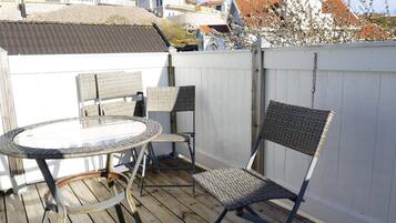 A deck with a glass-top table and wicker chairs, surrounded by a white fence.
