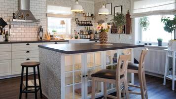 A kitchen with a central island, bar stools, a hanging light fixture, and a window with plants.