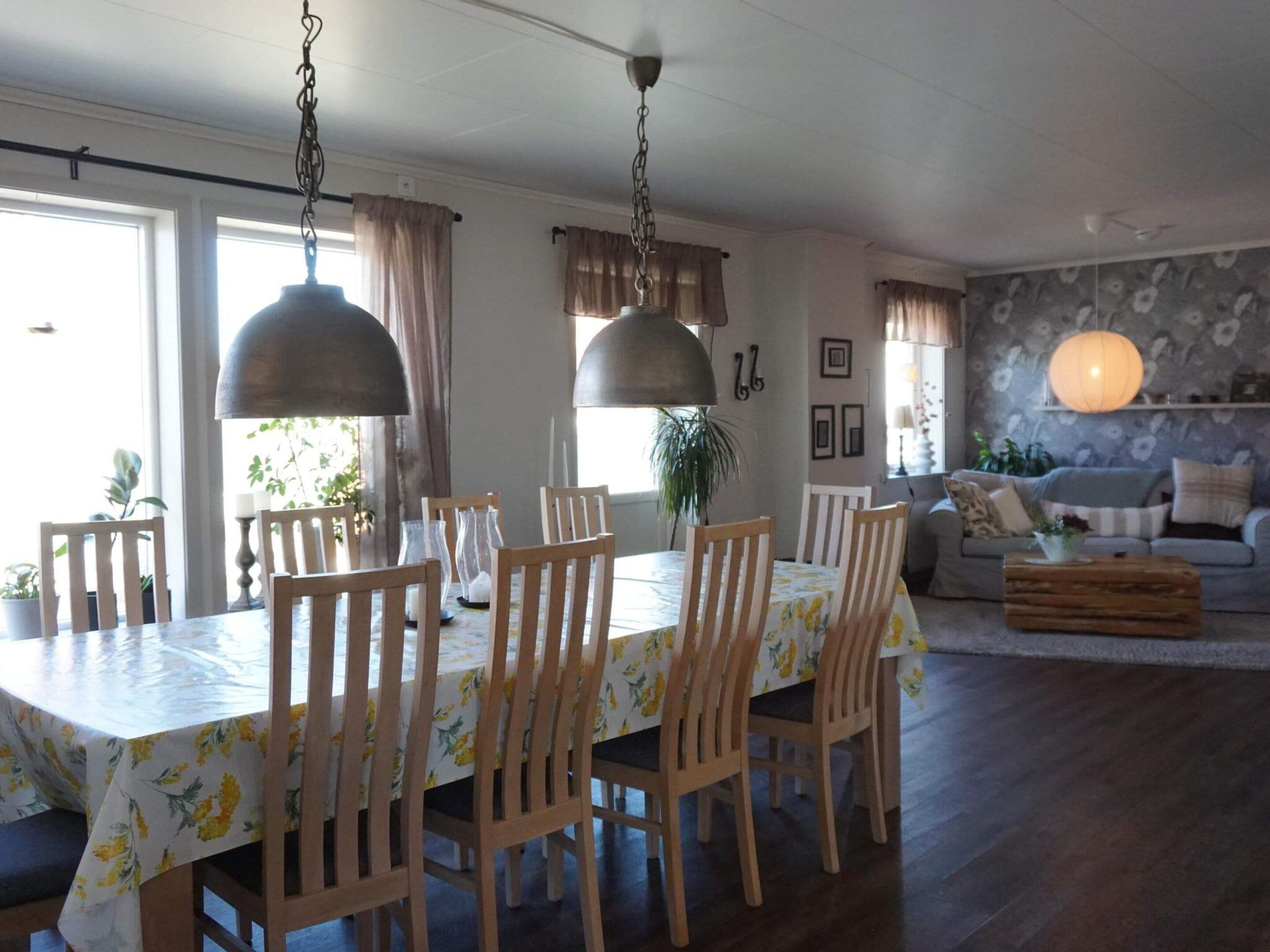 A dining area with a table set for six, surrounded by wooden chairs, and a sofa in the background.