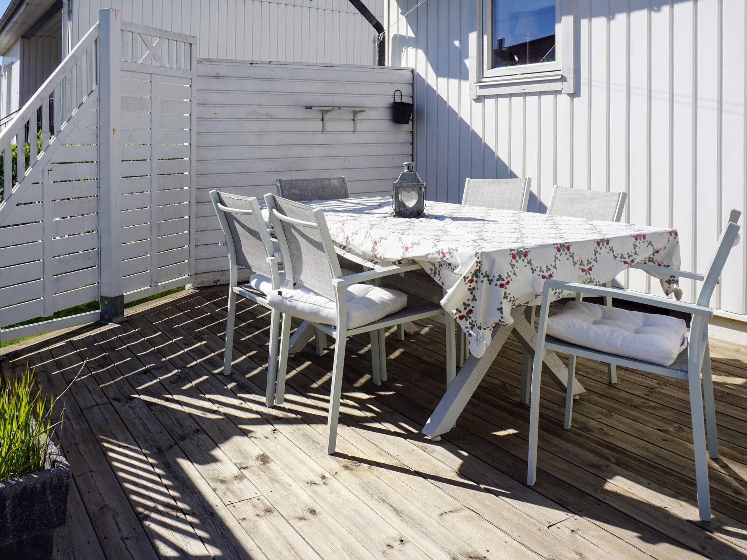 An outdoor patio with a table and chairs, a lantern, and a white fence.