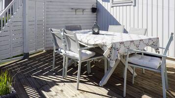 An outdoor patio with a table and chairs, a lantern, and a white fence.