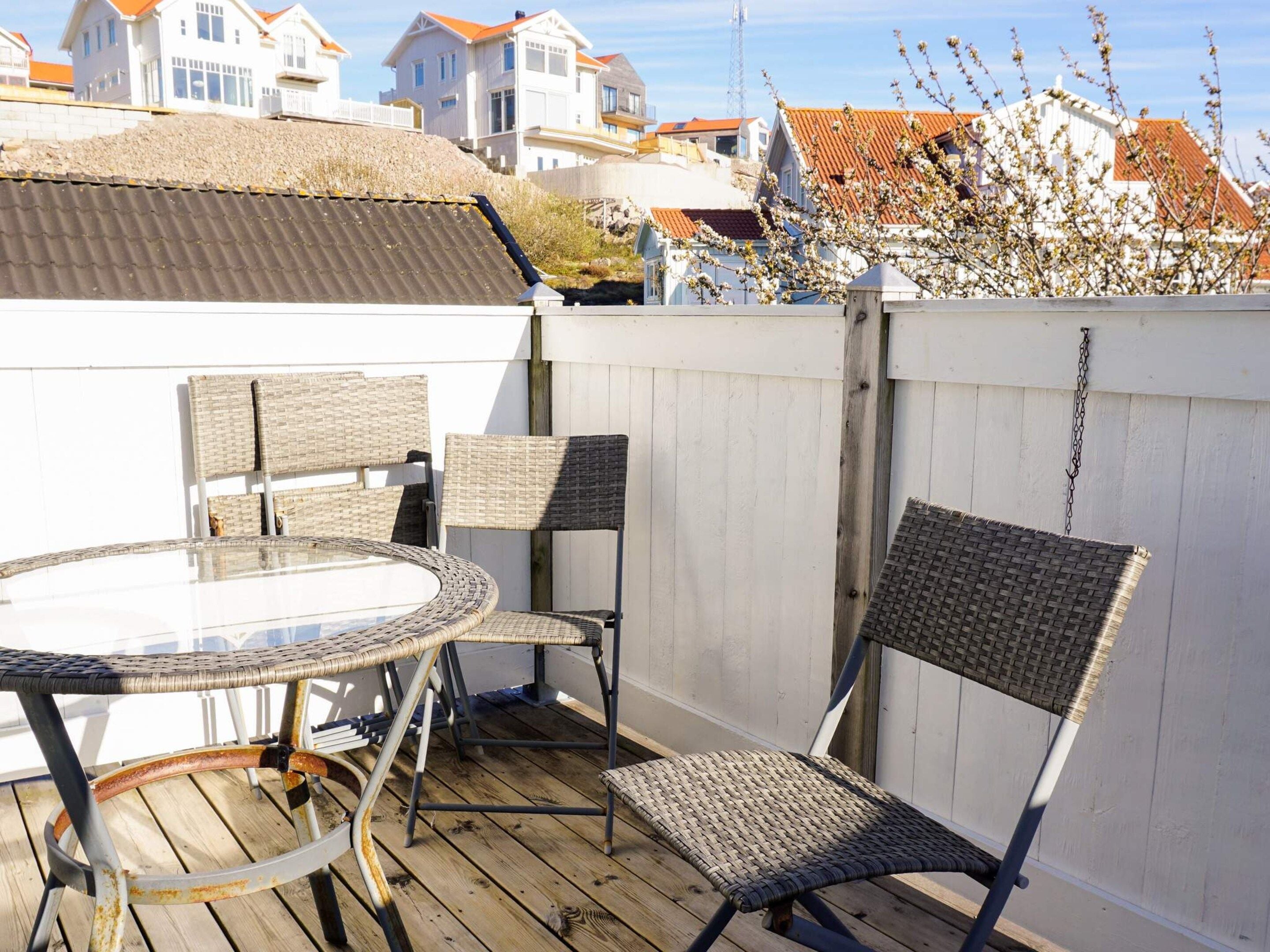 A wooden deck with a round glass table and wicker chairs, surrounded by a white fence.