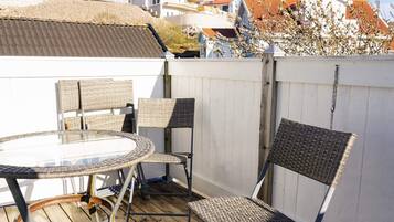 A wooden deck with a round glass table and wicker chairs, surrounded by a white fence.