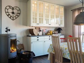 A cozy kitchen with a wood-burning stove, white cabinets, and a heart-shaped clock. - 4 Star Holiday Home in Kungshamn (Kungshamn)
