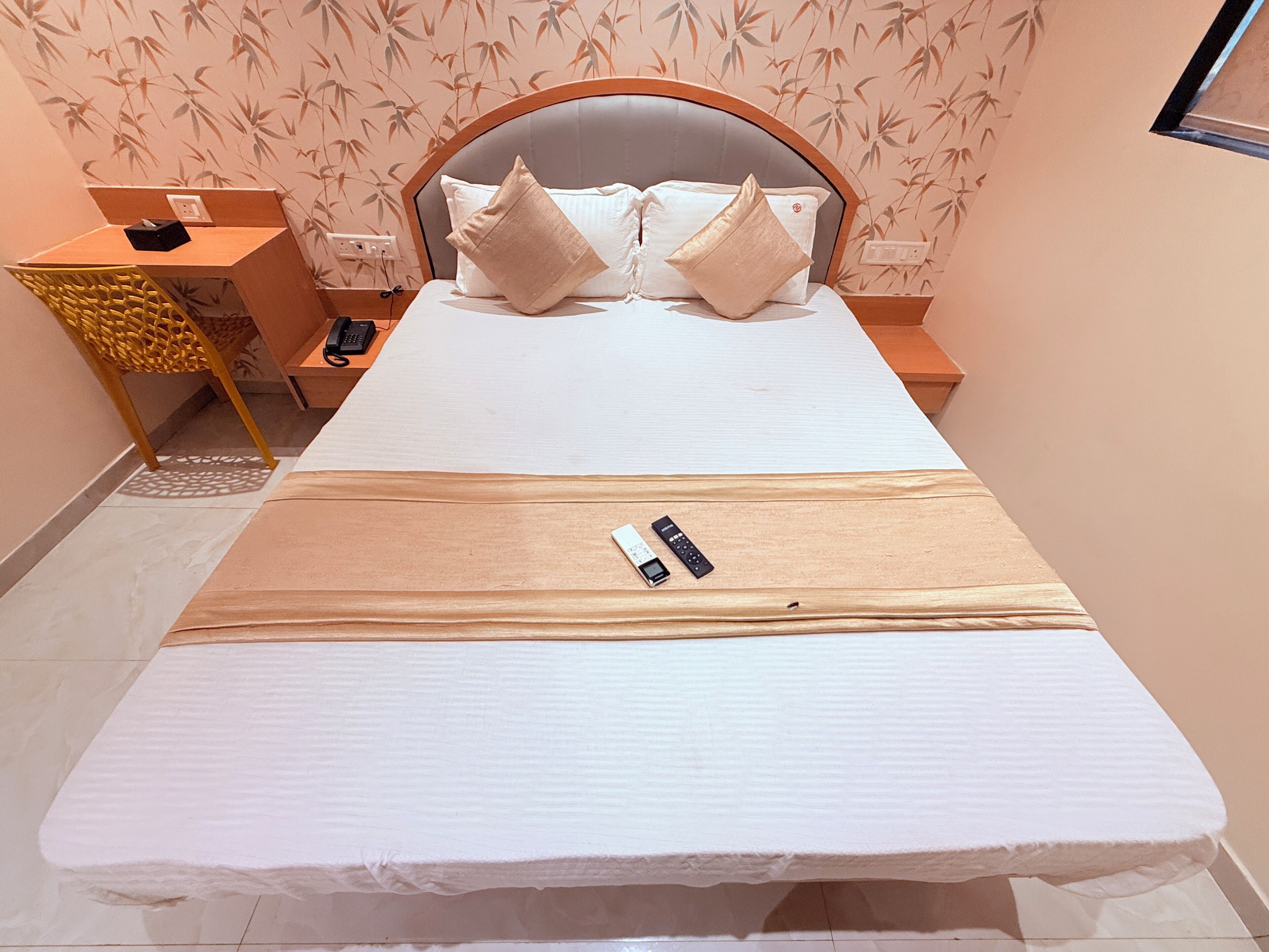 A neatly made bed with pillows, a bedside table with a phone, and a wall with bamboo wallpaper.