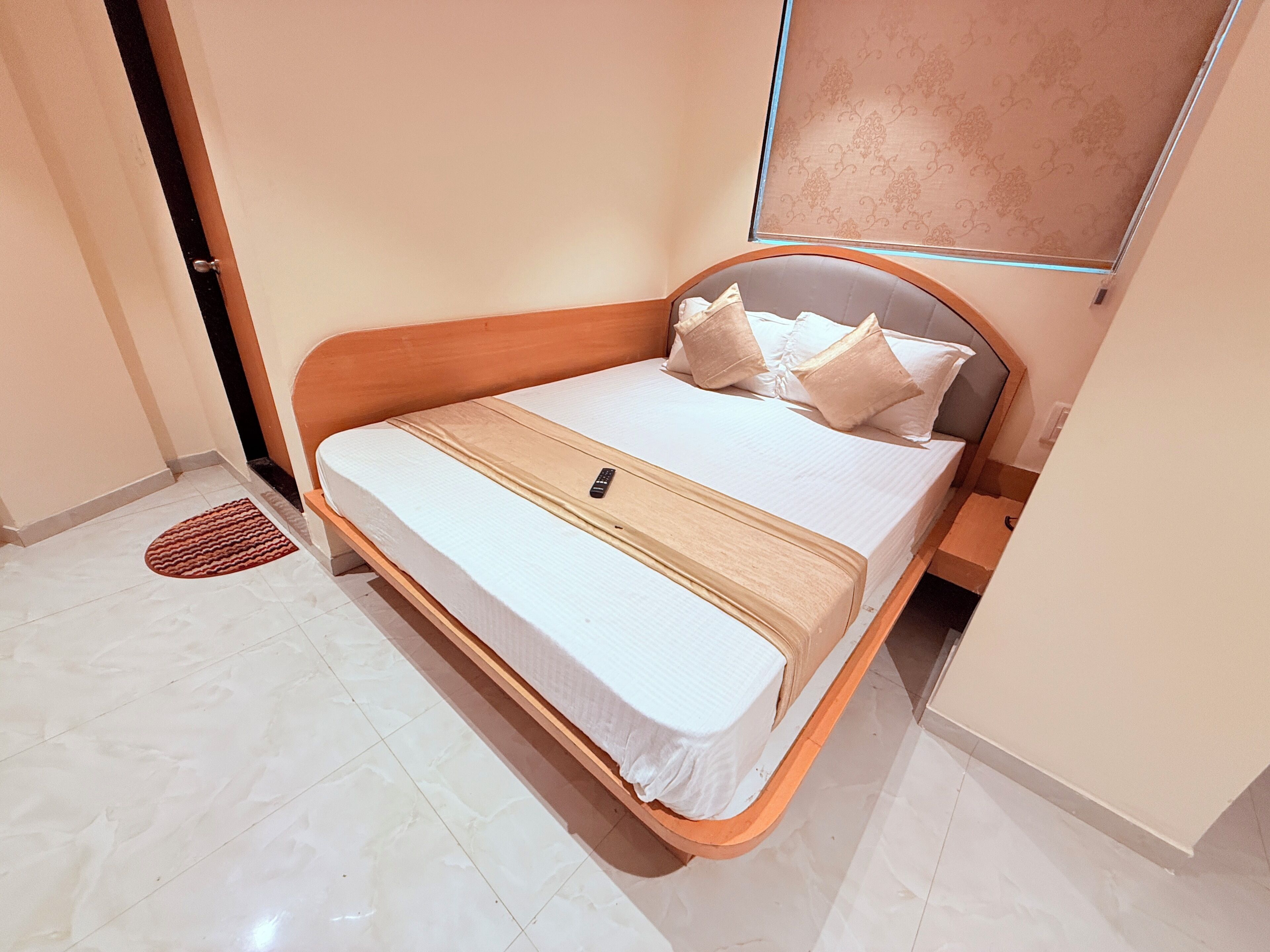 Uma cama com estrutura de madeira, roupa de cama branca e um controle remoto em cima.